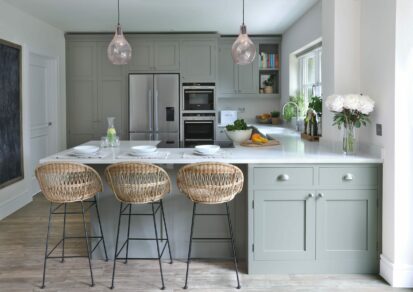 Molesey Painted Shaker Kitchen with a peninsula, rattan bar stools, pendant lights over induction hob, kitchen cabinets, American style fridge freezer in the background.