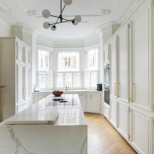 Highbury London panel and moulding kitchen with a sink in a bay window, kitchen island with a Bora downdraft hob, interesting pendant light above, decorative moulding in ceiling.