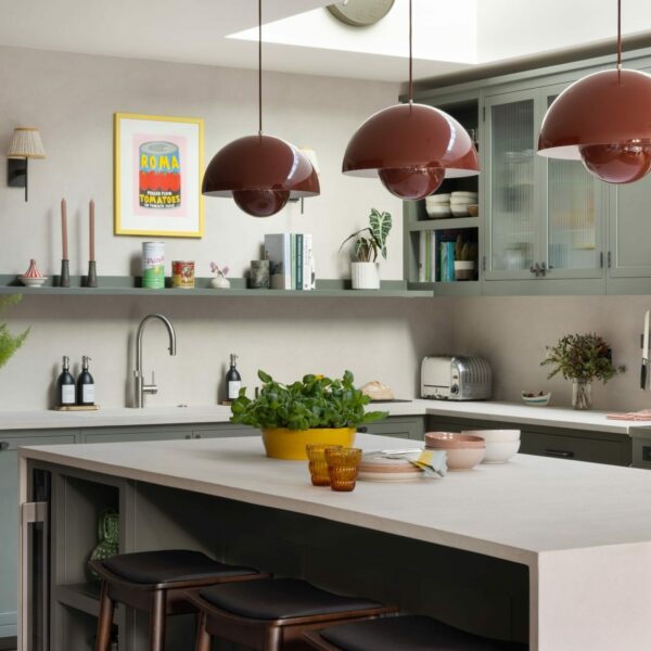 Modern shaker kitchen in dark grey-green with vermillion red flowerpot pendant lights over the island. Features micro-concrete worktops and open shelving.