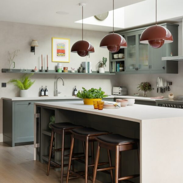 Modern shaker kitchen in dark grey-green with vermillion red flowerpot pendant lights over the island. Features micro-concrete worktops and open shelving.