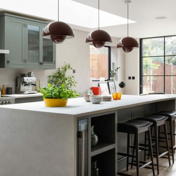 Shaker kitchen island with micro-concrete worktops, red pendant lights overlooking dining area with a large dining table, walnut chairs and a large green pendant above. Crittal style doors provide views and access to back garden.