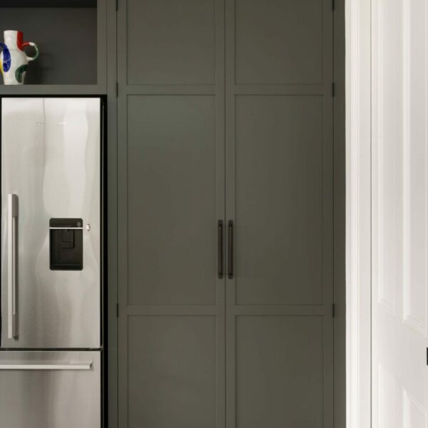 Shaker kitchen larder in a dark green-grey colour and dark bronze pull handles, next to a freestanding fridge freezer.