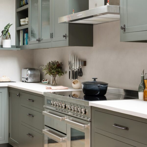 Shaker kitchen with a stainless steel Bertazzoni range cooker and a freestanding extractor above. Extractor flanked by wall cabinets, some with fluted glass.