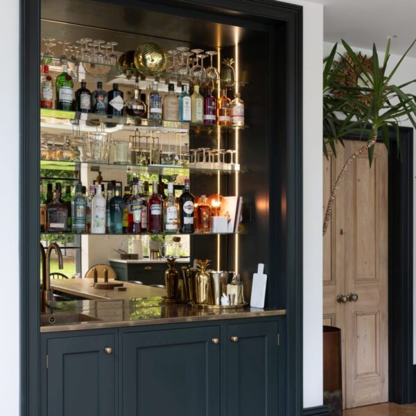 Shaker style bar cabinetry featuring an integrated undercounter fridge, a brass sink, and an antique mirror back panel behind glass shelves.