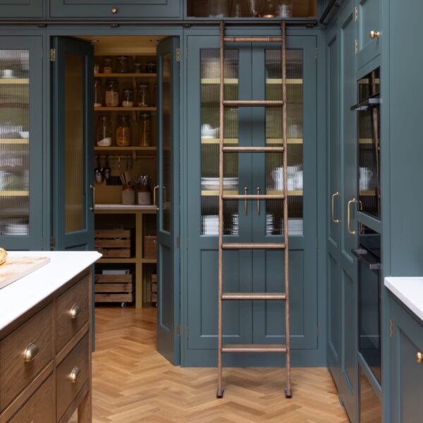 Green Shaker kitchen with larders featuring fluted glass doors and oak interiors. A matching pair of doors between the larders leads to a walk-in pantry. A ladder rail runs above the doors for access to top cabinets.