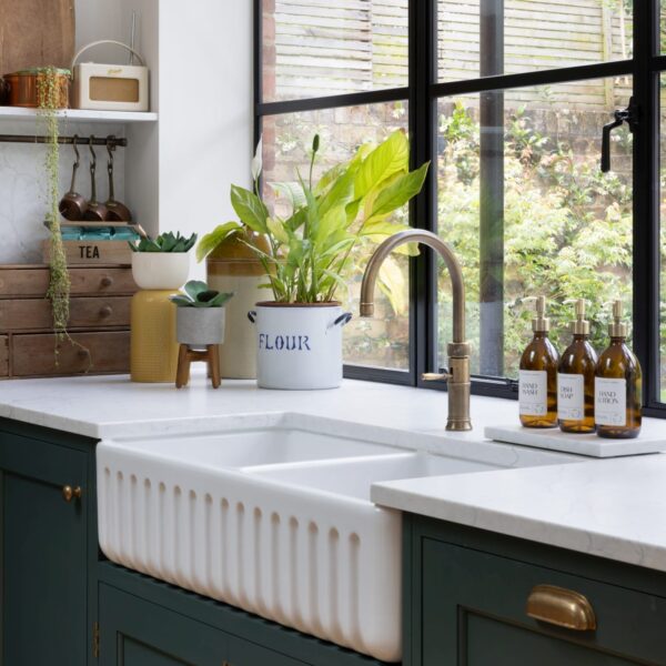 Ribbed Belfast sink positioned under large Crittall-style windows with black frames, offering lush green garden views.