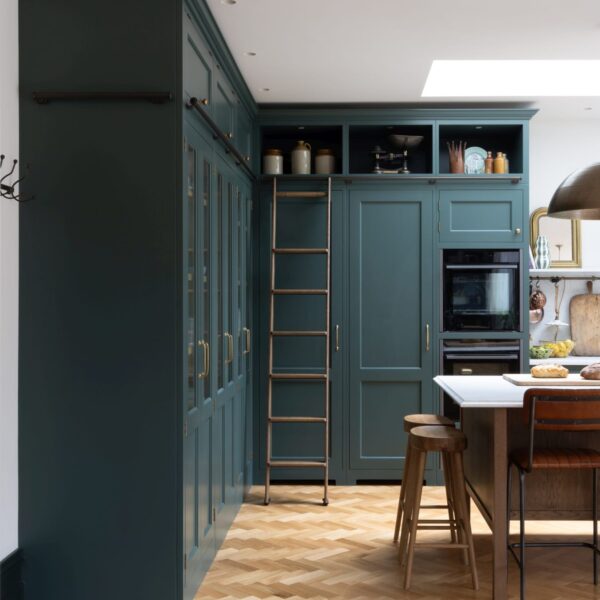 Tall cabinets in a green Shaker kitchen with a stained oak library ladder.