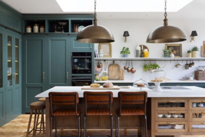 A green painted shaker kitchen with a stained oak island with leather bar stools with black metal legs and two wooden stools on the side.