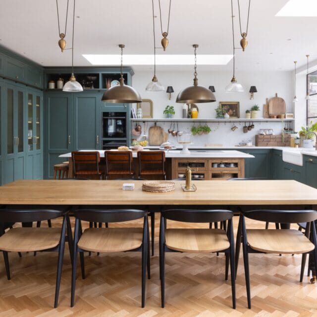 Green Shaker kitchen with a stained oak island, leather bar stools and a large oak dining table with black and oak dining chairs,.