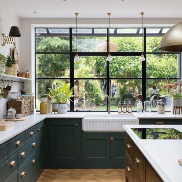Ribbed Belfast sink positioned under large Crittall-style windows with black frames, offering lush green garden views. A vented Bora hob sits on top of a stained oak island.