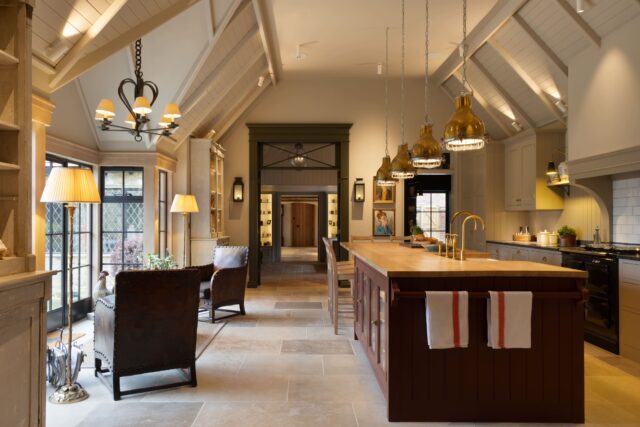 Open-plan bespoke handmade kitchen with vaulted beamed ceiling, plum island, brass pendant lights and country living area, Haslemere Surrey by Higham Furniture