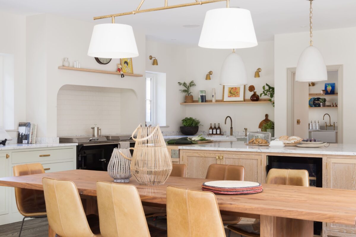 Open-plan kitchen in a north-facing room with sage green cabinets, natural oak island, warm brass pendant lights, and open shelving — light-enhancing colour scheme for a period home