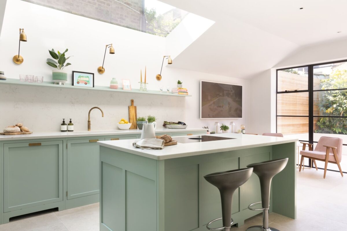 Sage green shaker kitchen with white quartz worktops, brass hardware, open shelving, and large roof lantern — ideal cabinet colour for a north-facing Victorian kitchen extension