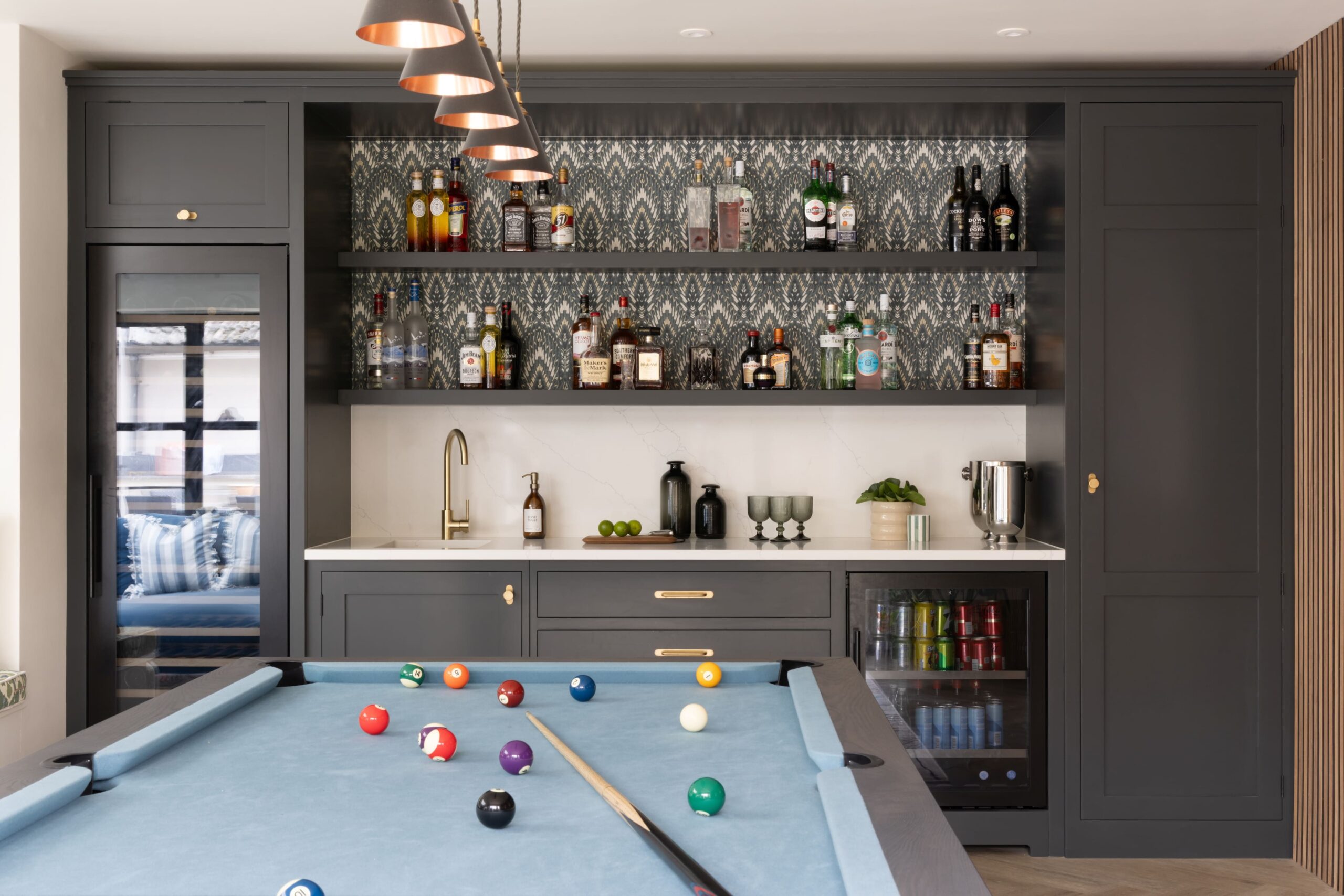 Bespoke home bar with dark cabinetry, drinks display shelving and integrated storage next to pool table