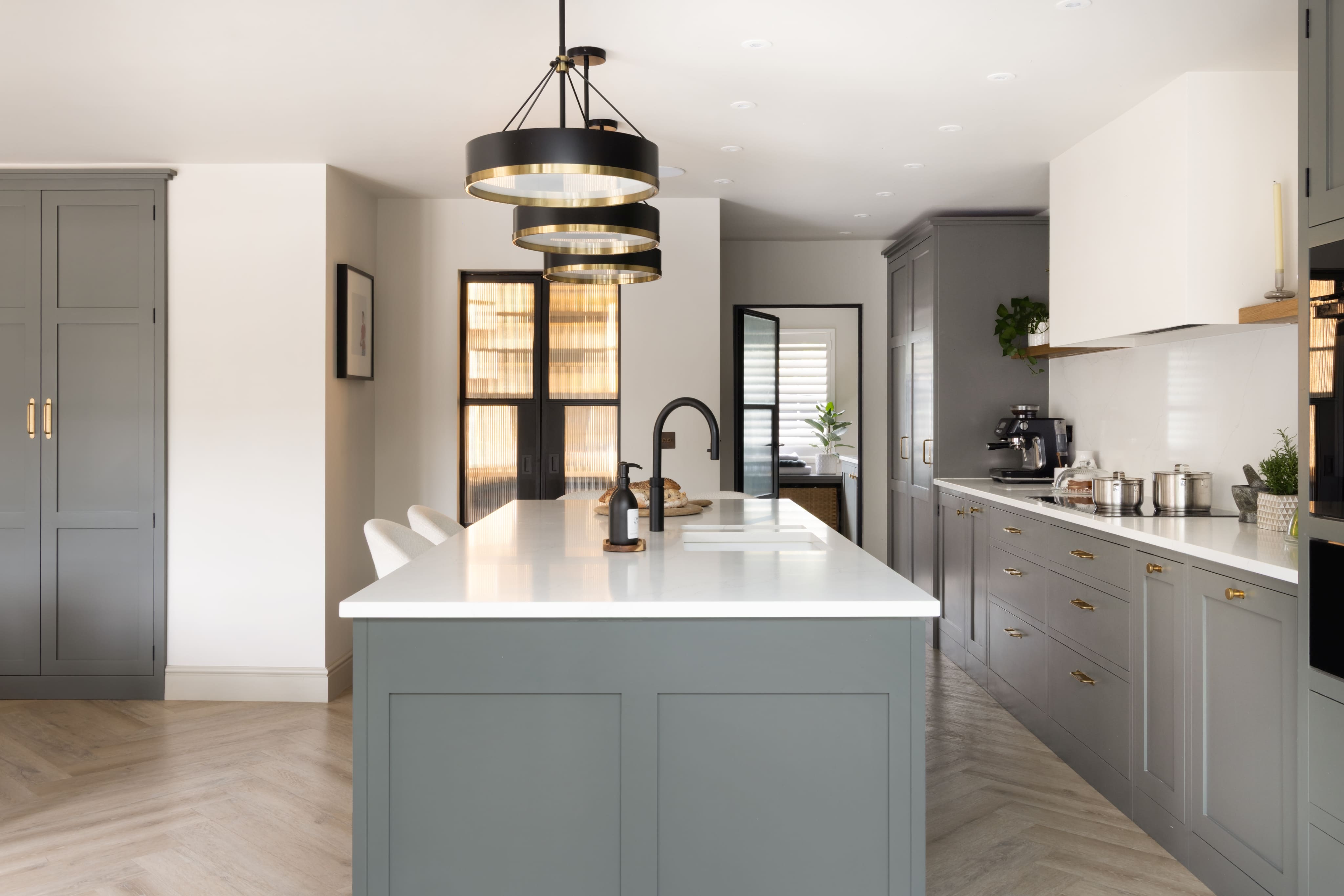 White quartz worktop on sage green kitchen island with black and brass pendant lighting