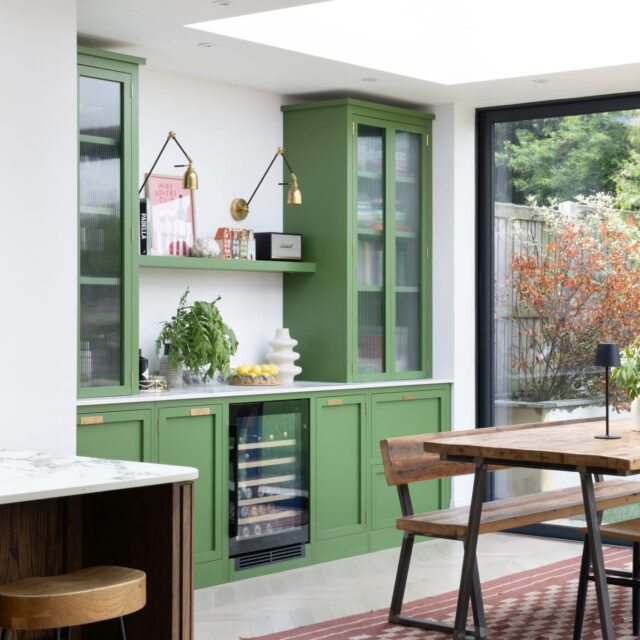 Bespoke green kitchen cabinetry fitted around a bright dining area with garden views