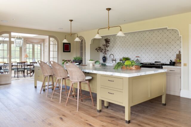 Traditional painted kitchen with soft yellow island, bar stools and marble worktop in a spacious family home