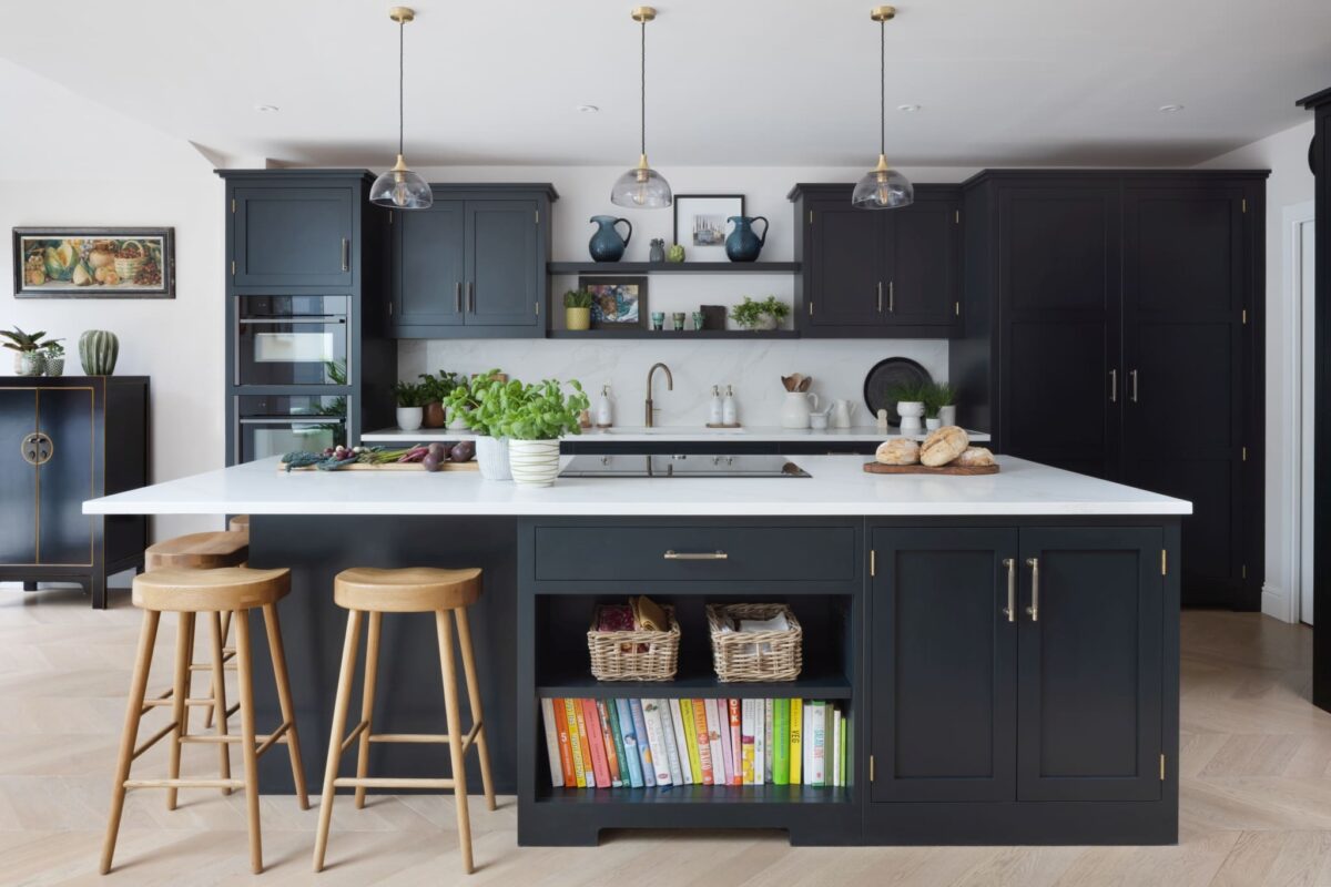 Dark navy shaker kitchen with brass cup handles and pull handles, brass pendant lights, and white marble worktop
