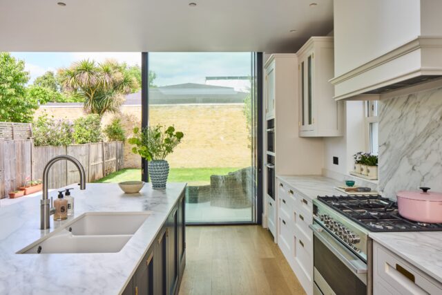 Handmade kitchen with marble worktops, integrated sink and large glass doors opening to garden view